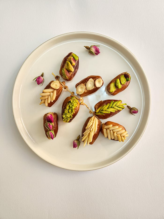 A plate of gourmet stuffed dates with pistachios, almonds, and rosebuds elegantly arranged on white.